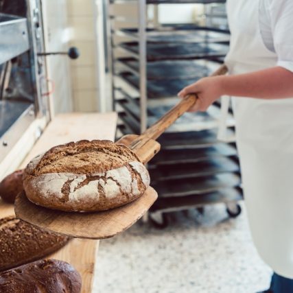 Woman in bakery putting bread on board with baking shovel
